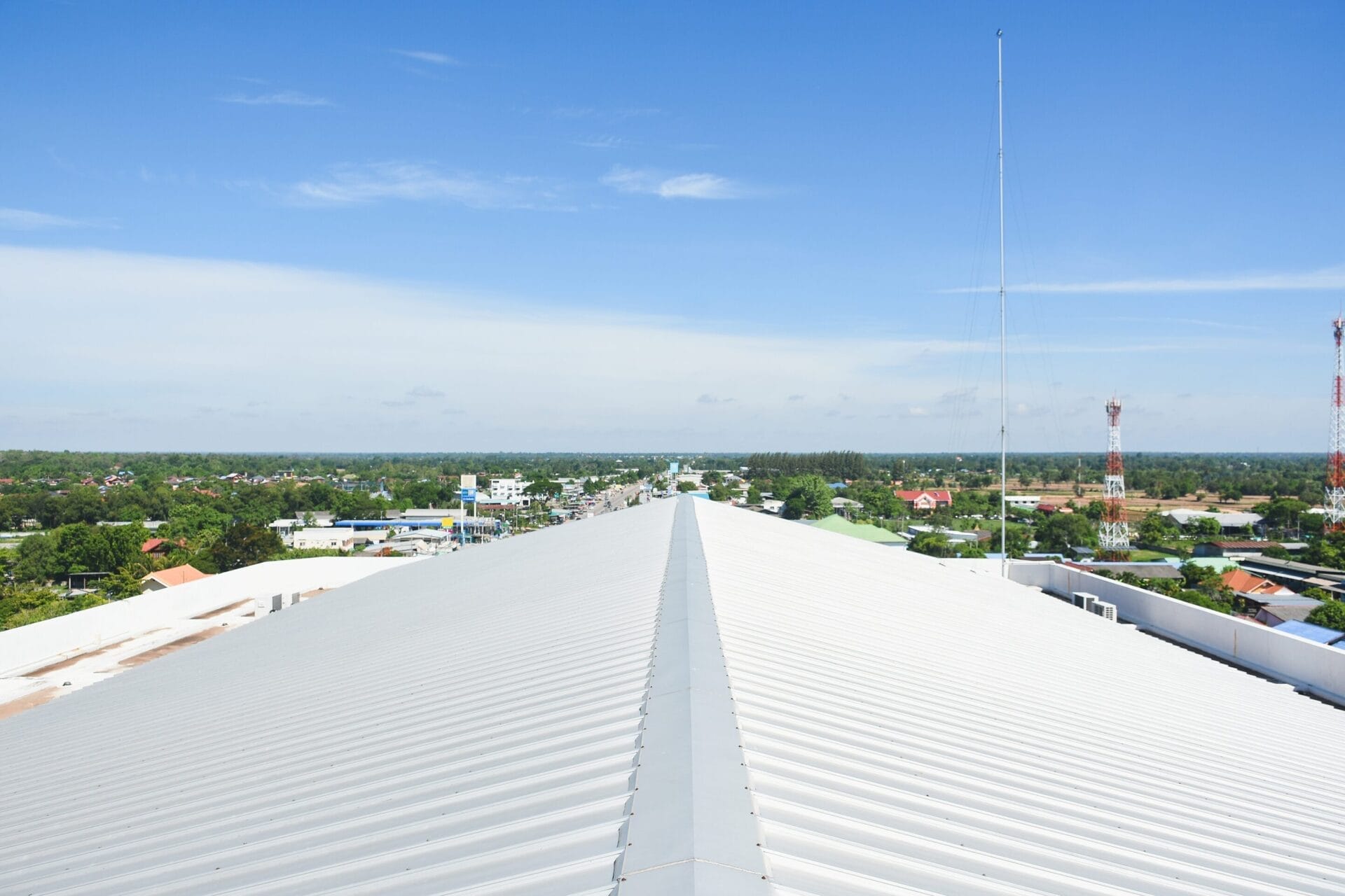 View from a white roof overlooking a town with scattered buildings, roads, and tall antennas under a clear blue sky.