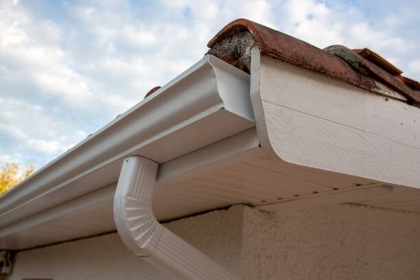 Close-up view of a newly installed white seamless gutter and downspout system attached to the white fascia board of a house.